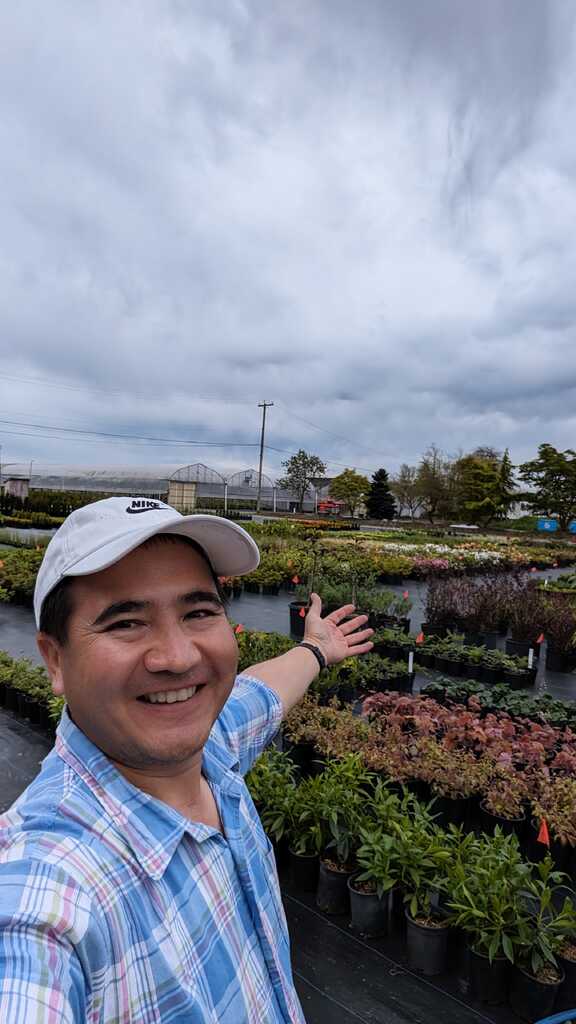 Reza standing in a nursery with rows of plants.